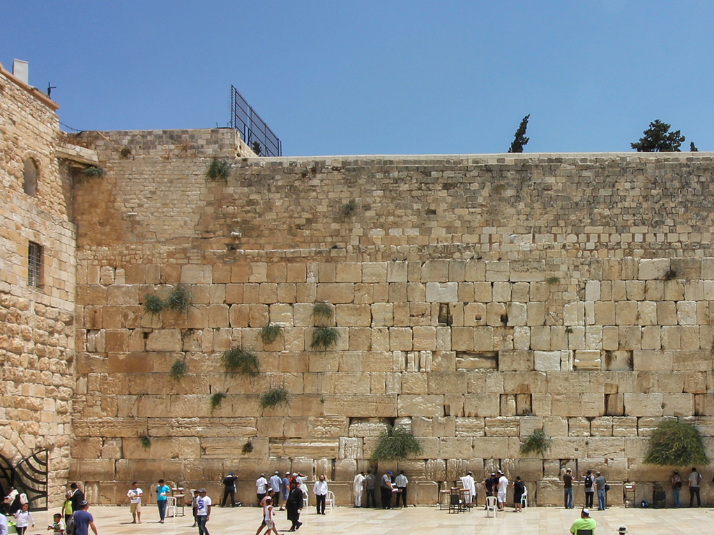 Visitors line up against the high stone wall in prayer.