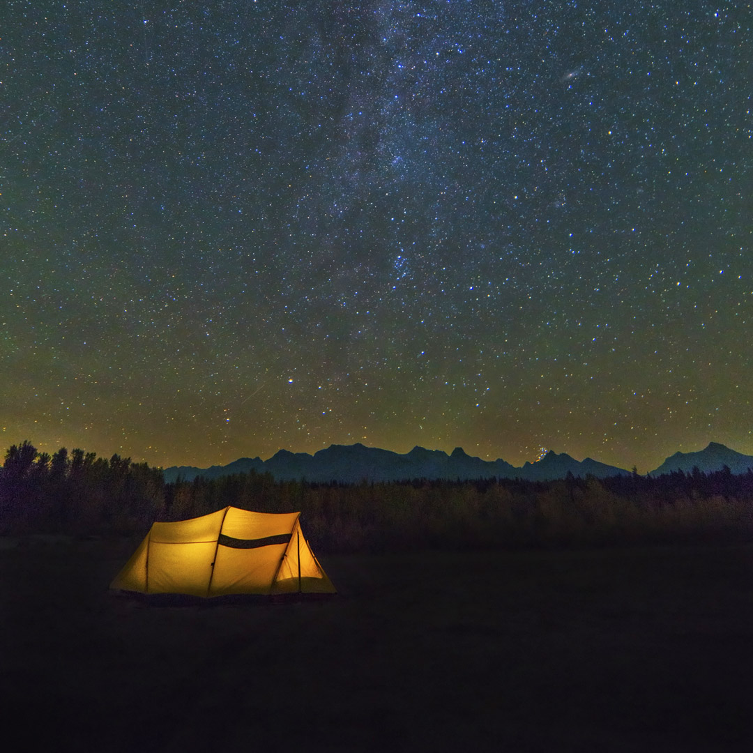 yellow tent lit up at night with stars above