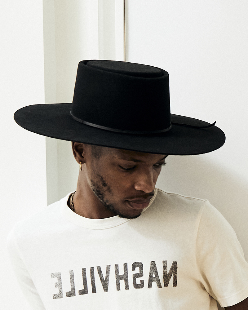 Head shot of a man wearing a white t-shirt printed with the word "Nashville" and a black wool felt hat with a flat top and wide brim