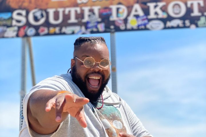 happy black plus size man in front of a South Dakota sign