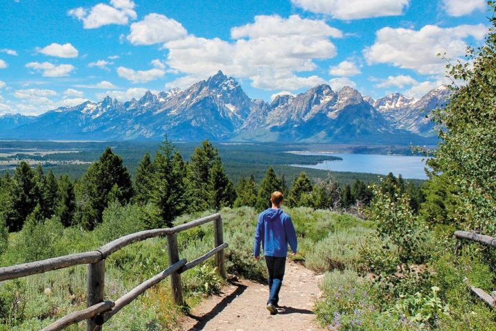 person in blue hoodie walking on a nature trail with mountains in the distance